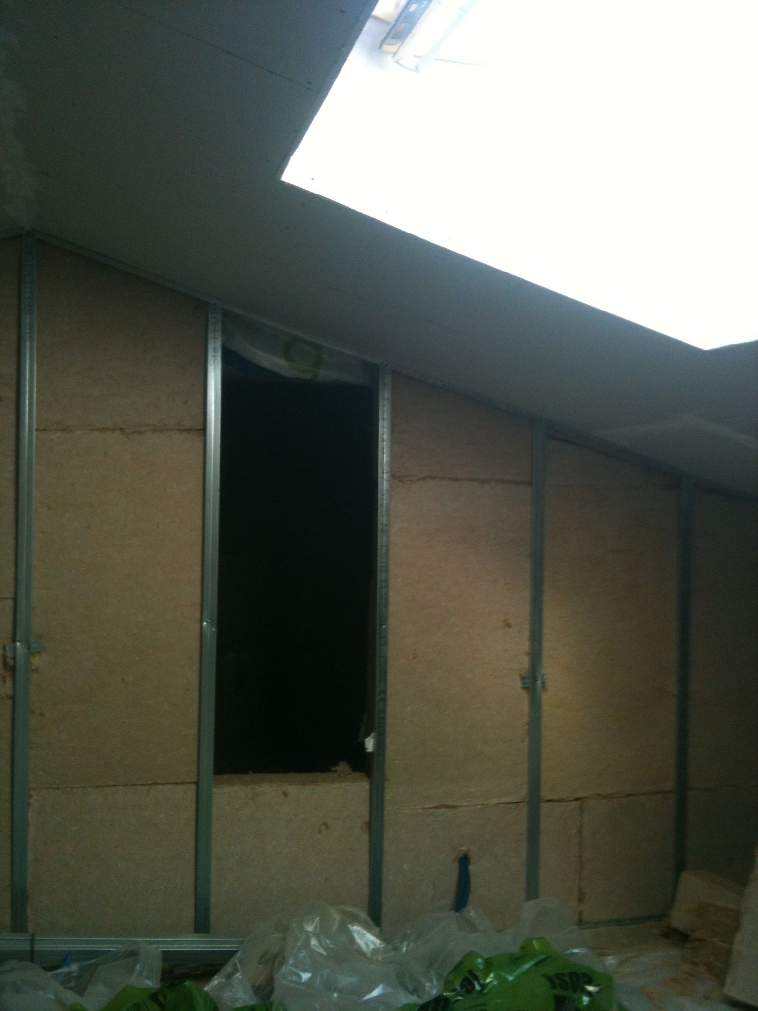 Vue intérieure d'un grenier avec charpente métallique et panneaux isolants installés; une ouverture sombre et un puits de lumière.