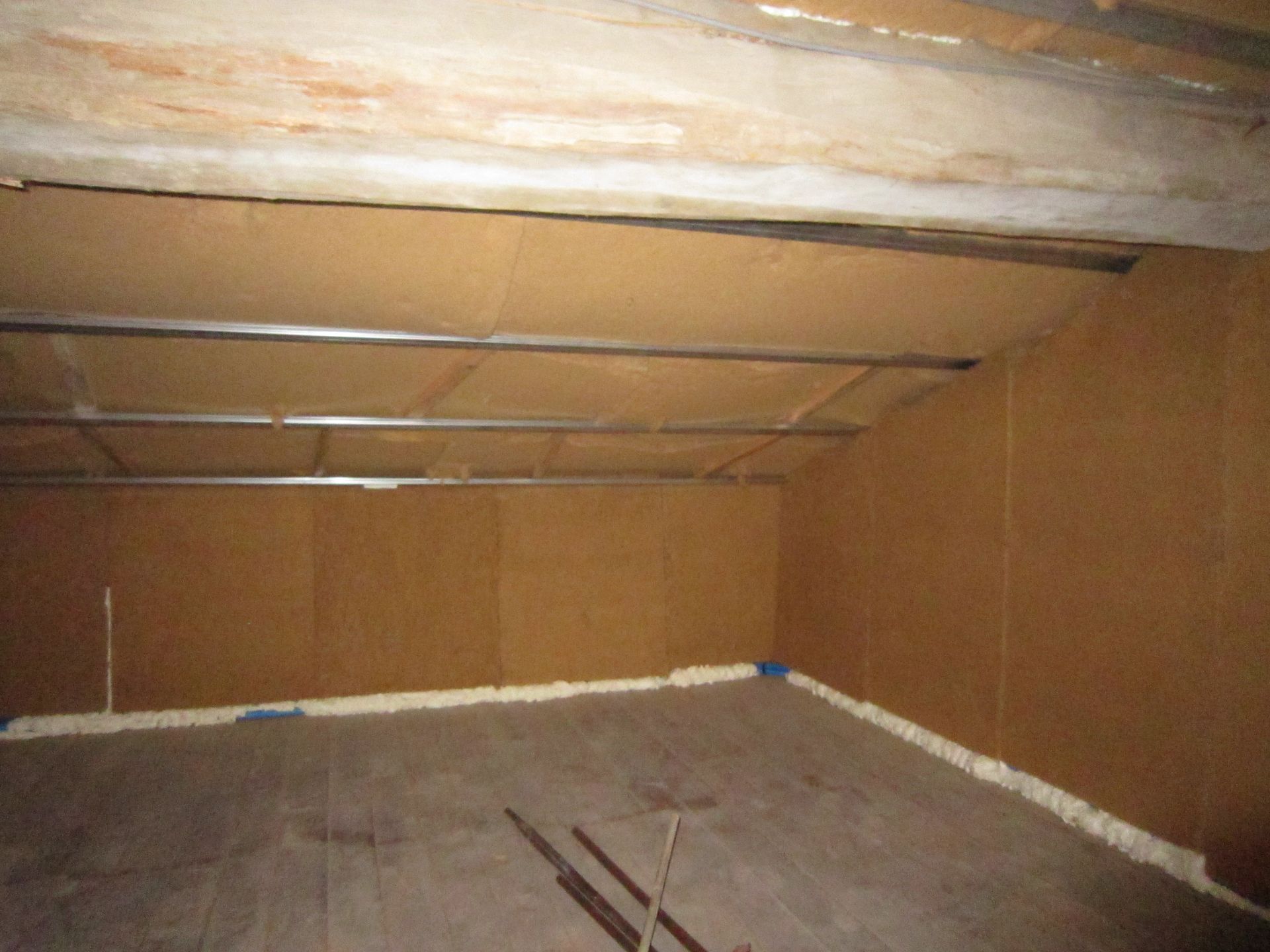 Vue intérieure d'un grenier inachevé avec des murs bruns, un plafond gris et un plancher en bois.