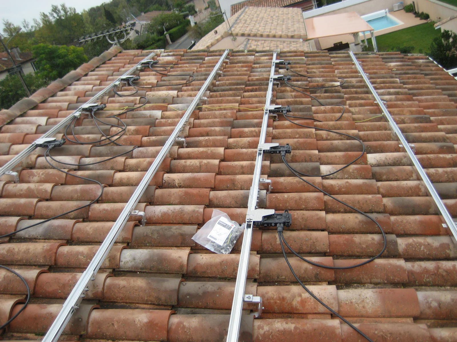 Installation de panneaux solaires sur un toit en tuiles rouges ; rails et composants électriques sont visibles.