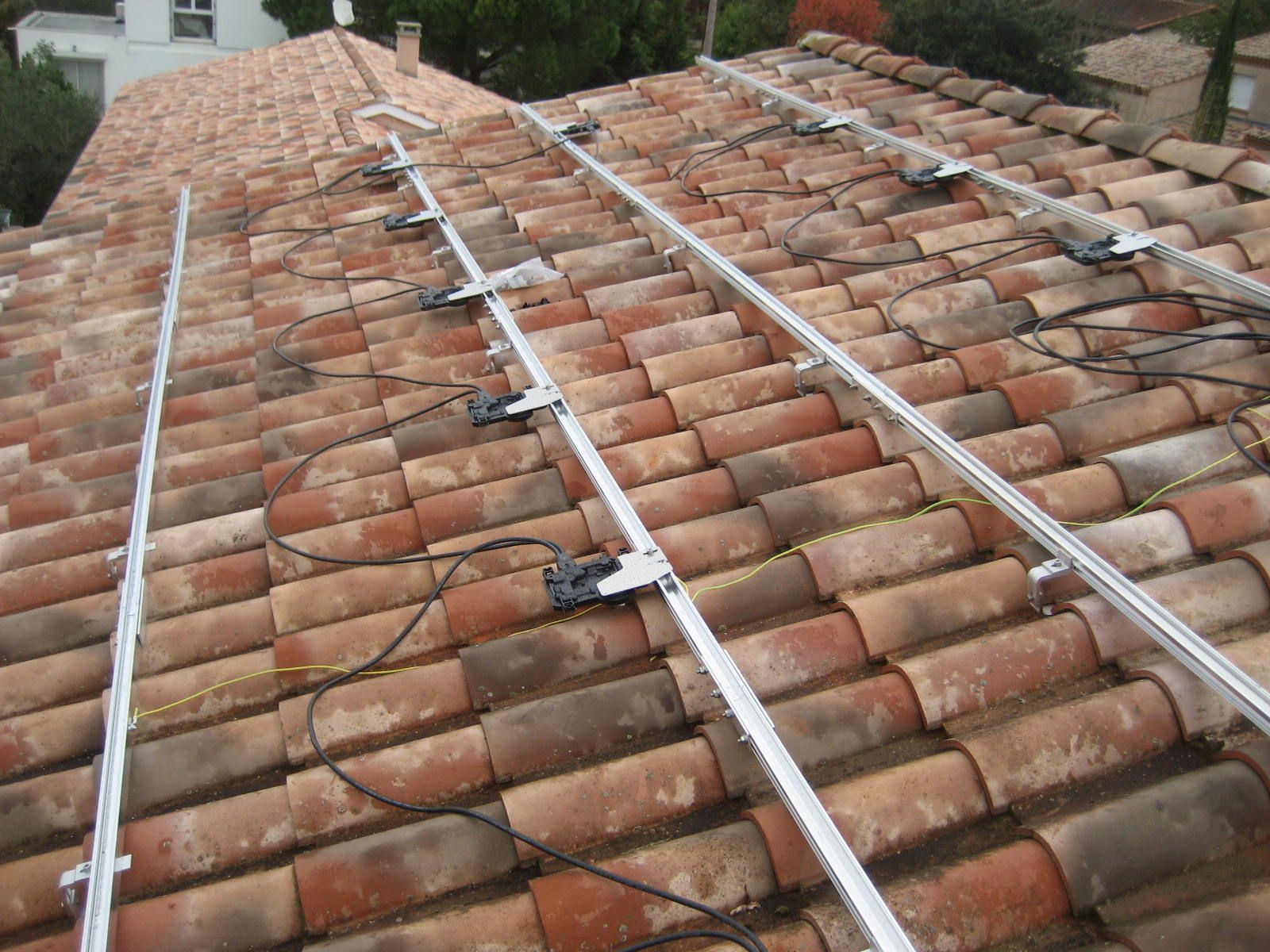 Rails de montage de panneaux solaires en cours d'installation sur un toit en tuiles en terre cuite.
