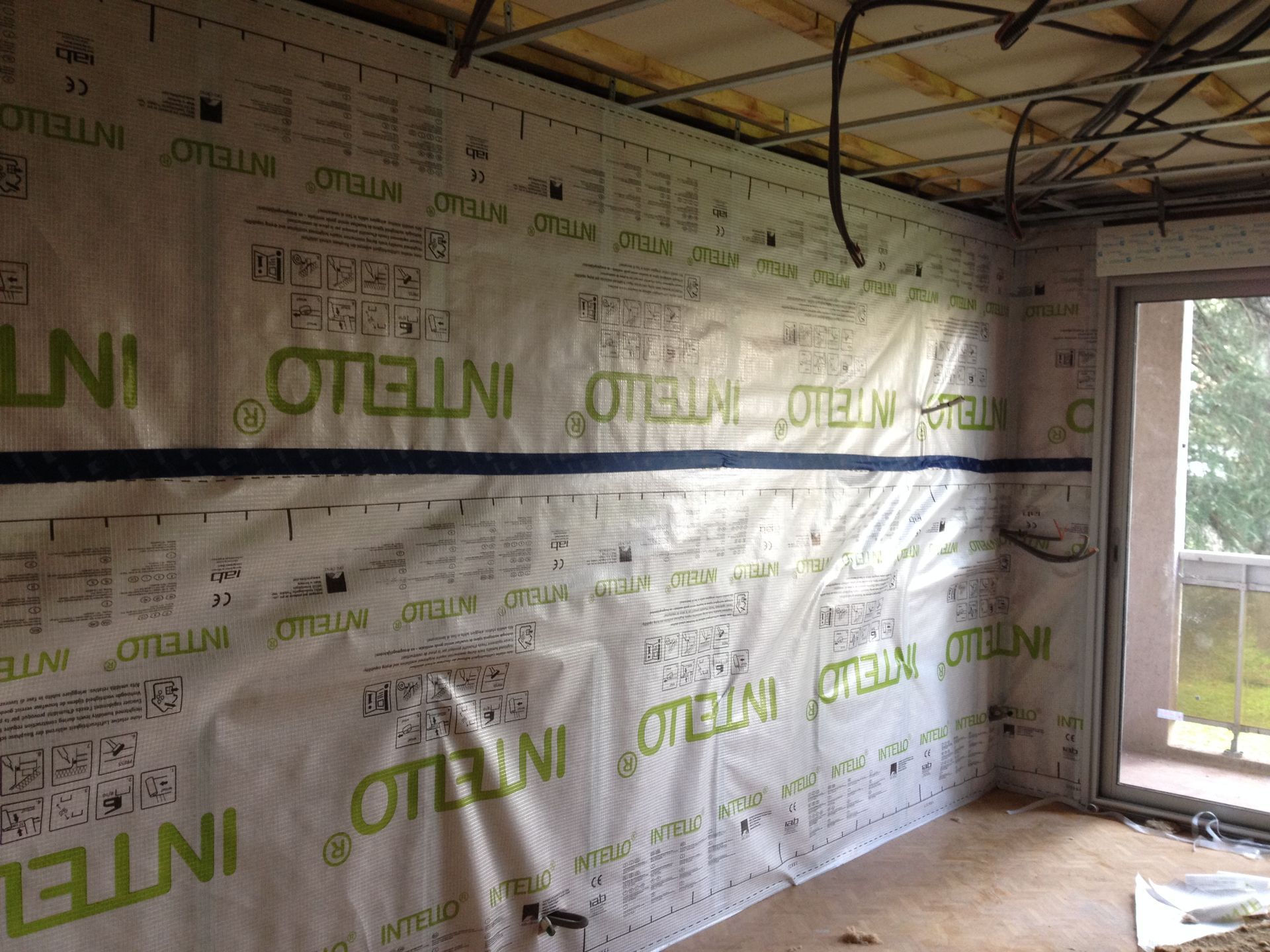 Pièce intérieure en construction avec pare-vapeur sur les murs, câblage et plafond exposé.