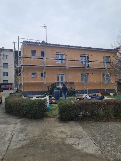 Extérieur d'un bâtiment avec échafaudages, ouvriers et murs jaunes, près d'un trottoir et de buissons.