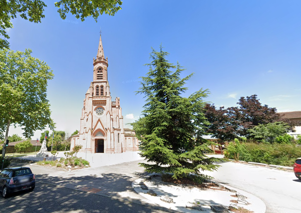 Église avec un haut clocher, des arbres et un ciel bleu.