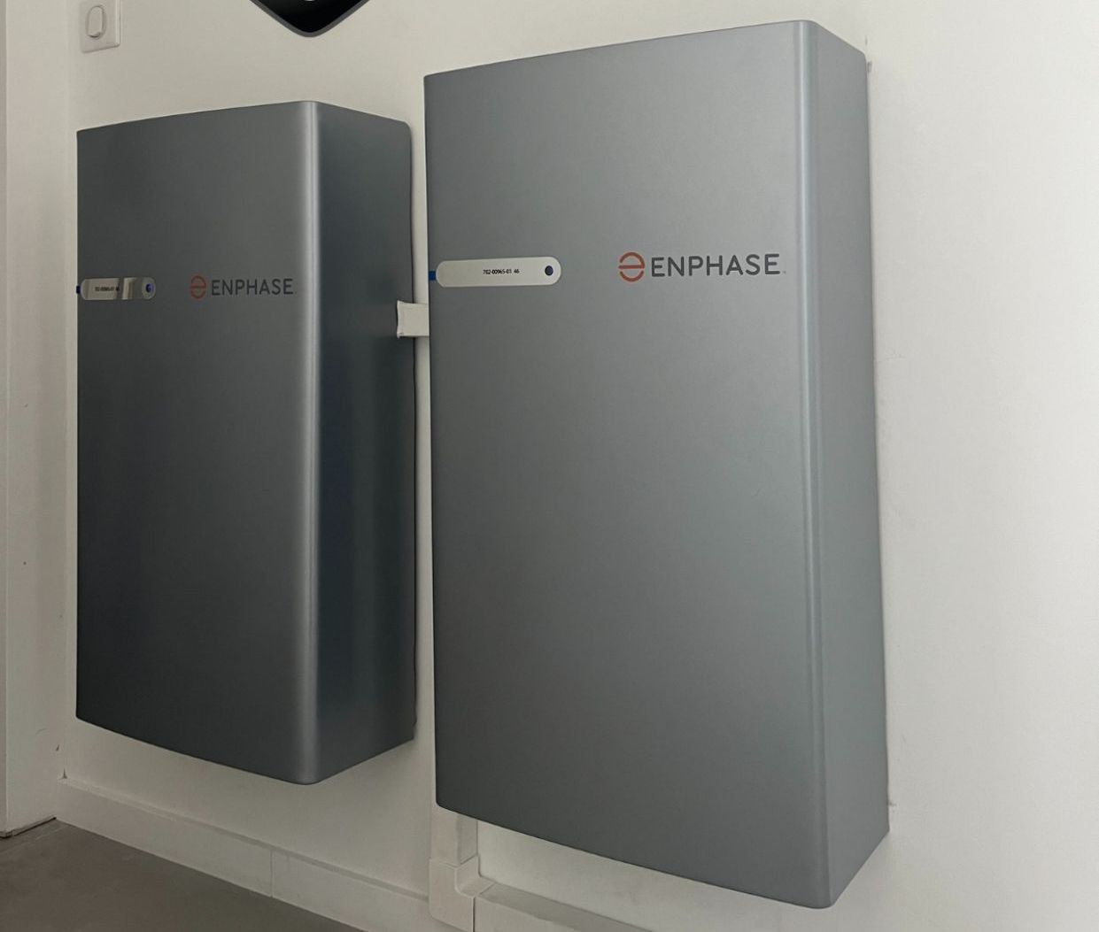 Deux unités de batterie Enphase grises montées sur un mur blanc.