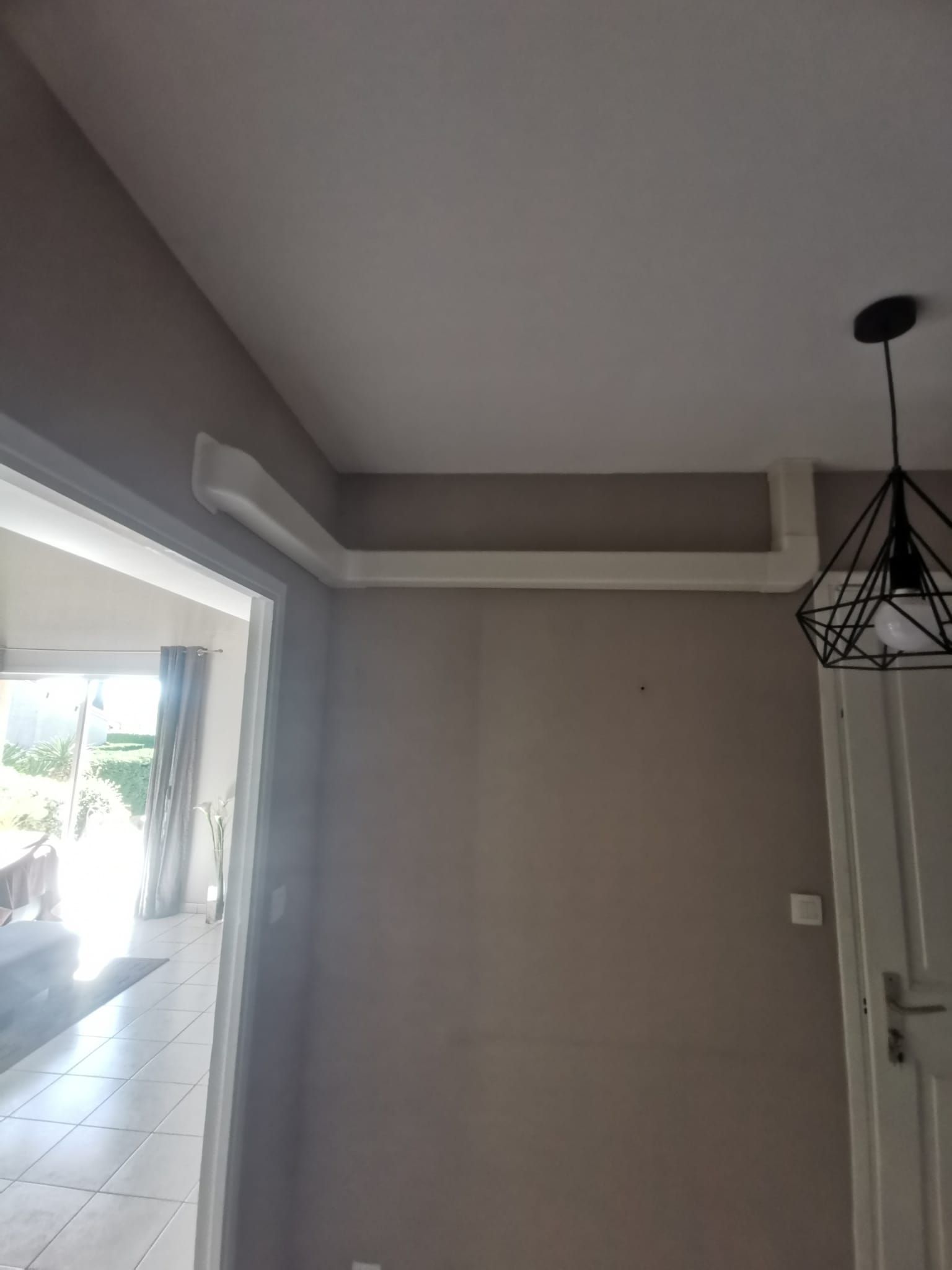 Vue intérieure : mur gris, moulure blanche, porte et luminaire suspendu.