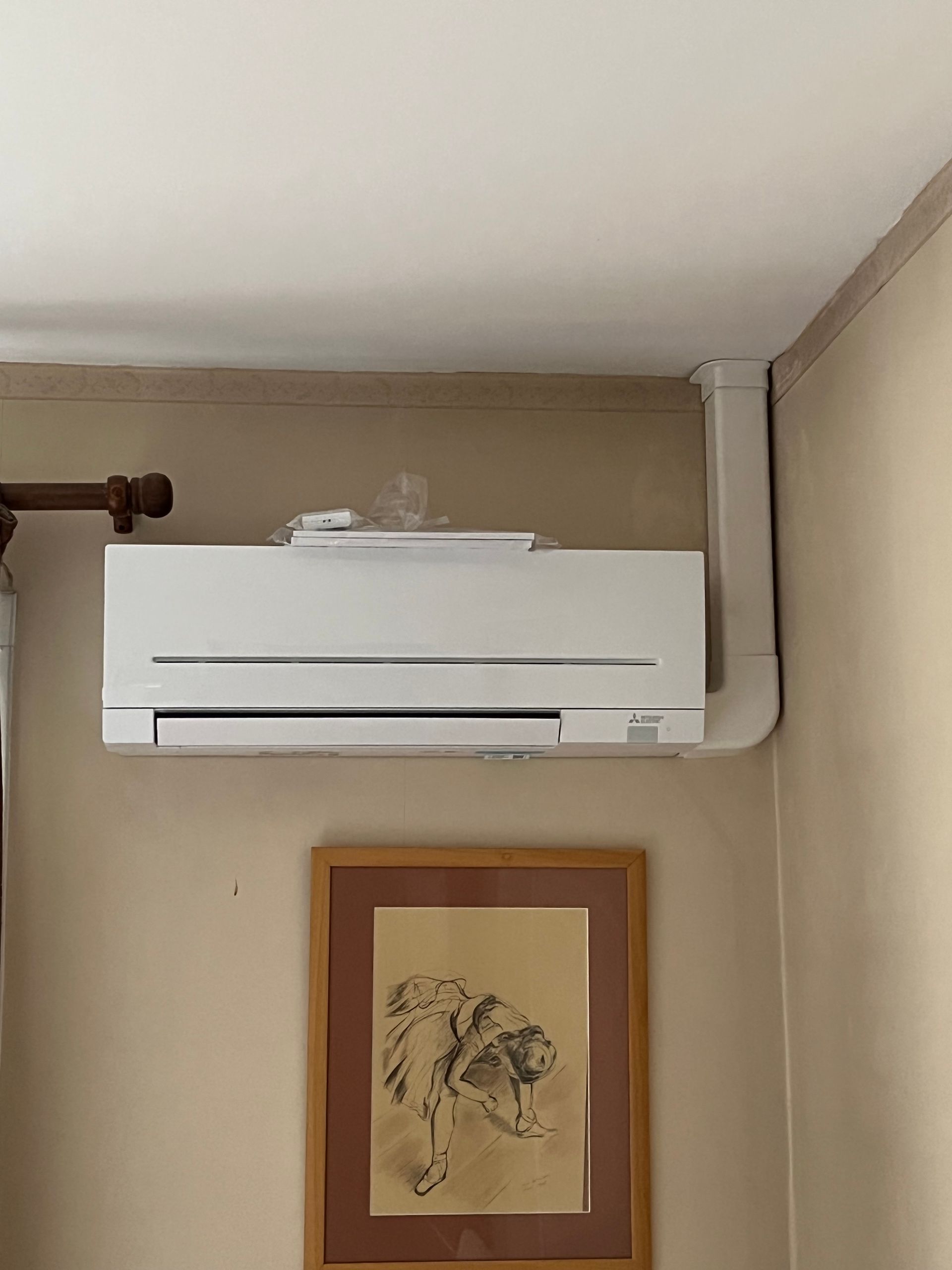 Climatiseur blanc monté sur un mur au-dessus d'un dessin encadré, près d'un coin et du plafond.