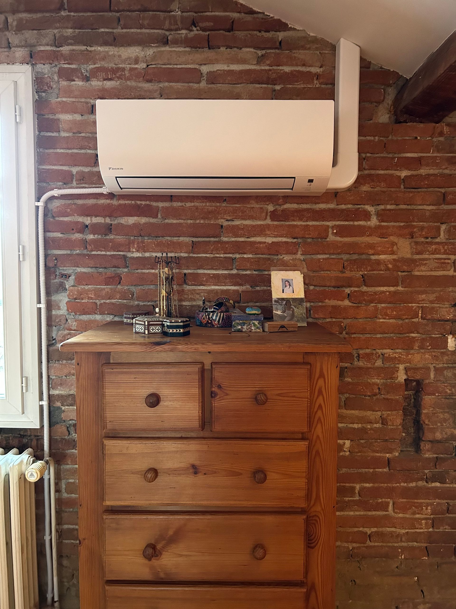 Unité de climatisation montée sur un mur de briques rouges au-dessus d'une commode en bois.