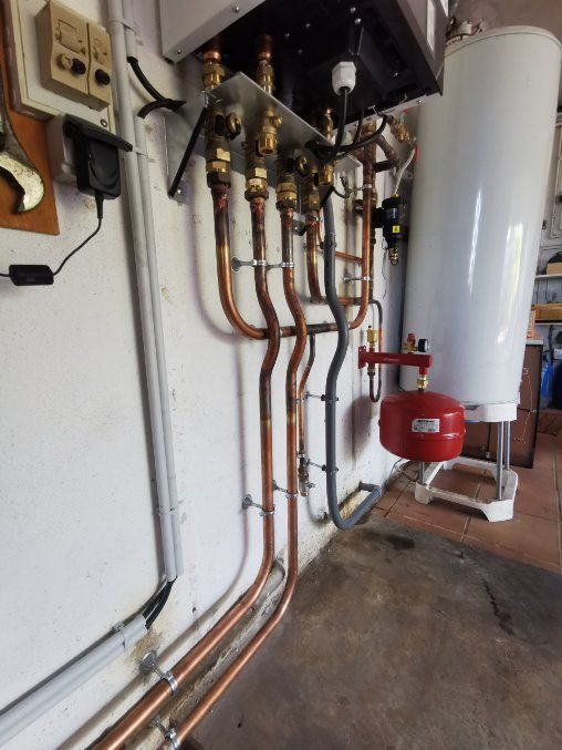 Tuyaux en cuivre reliés à une chaudière et à un réservoir d'eau blanche sur un mur.