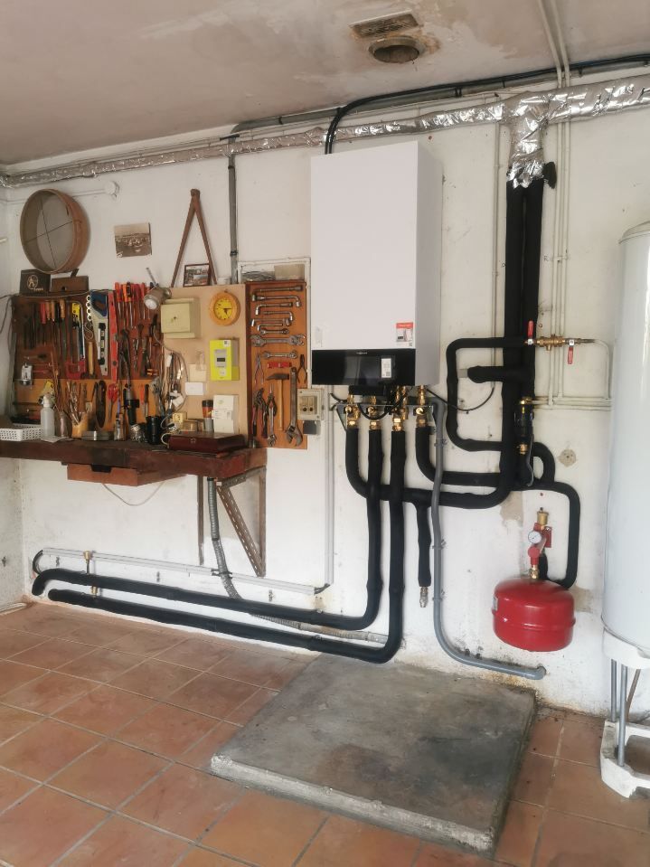 Atelier avec un système de chauffage blanc, des outils au mur, des tuyaux isolés noirs et un vase d'expansion rouge.