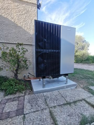 Pompe à chaleur grise à l'extérieur d'un bâtiment beige sur une dalle de béton.