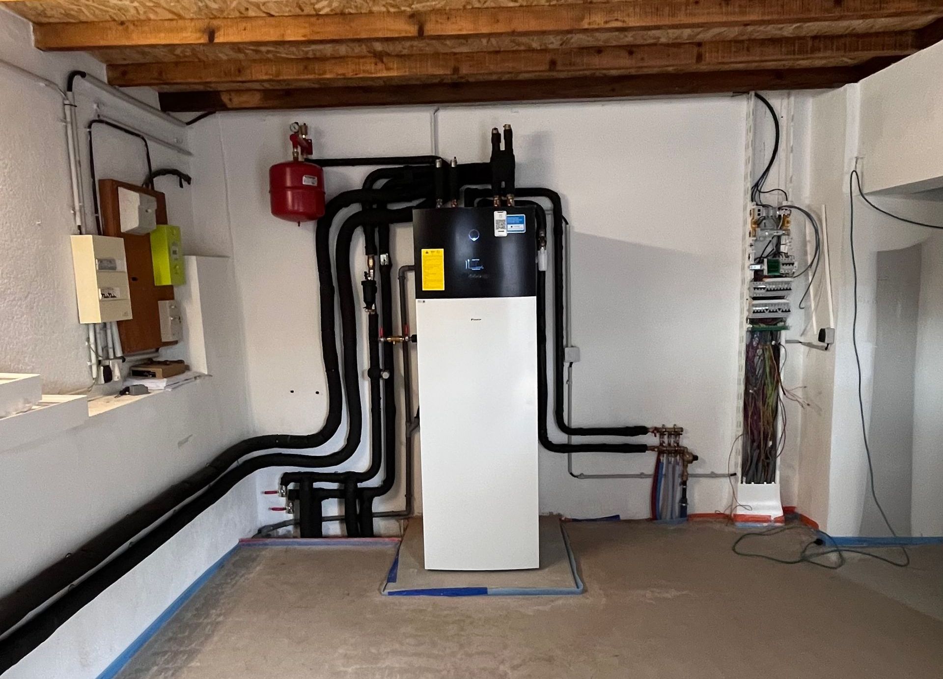 Système de thermopompe dans un sous-sol, avec tuyaux et composantes électriques sur les murs.