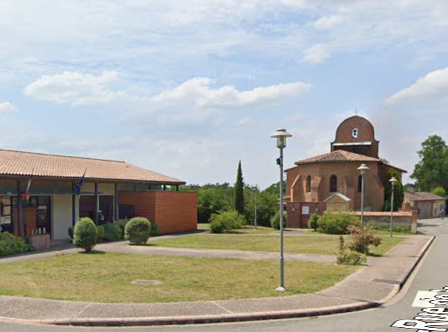 Une église en briques avec un toit en forme de dôme se trouve à côté d'un bâtiment bas dans une zone herbeuse par une journée ensoleillée.