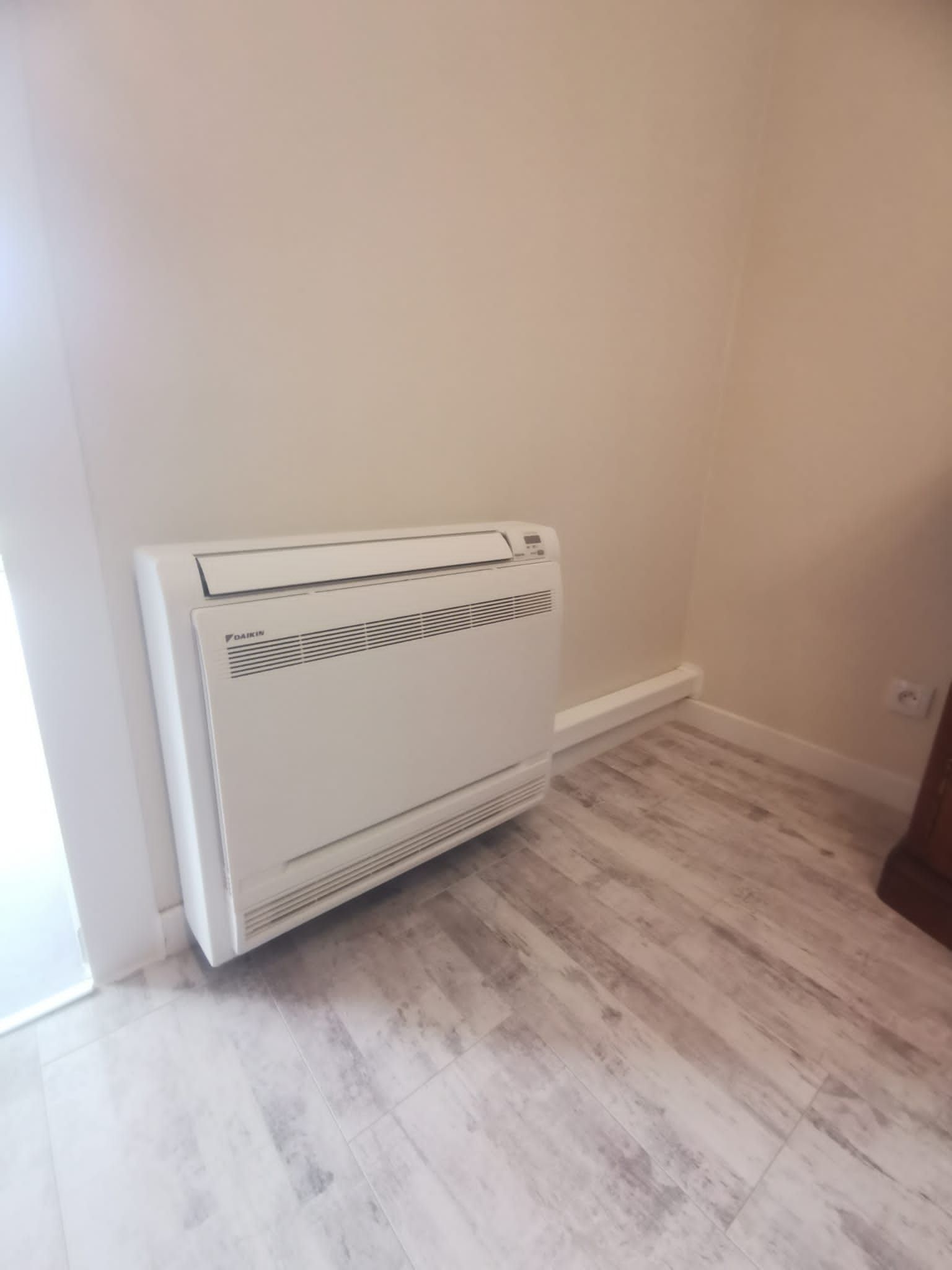 Chauffage mural blanc dans un coin d'une pièce avec sol gris clair.