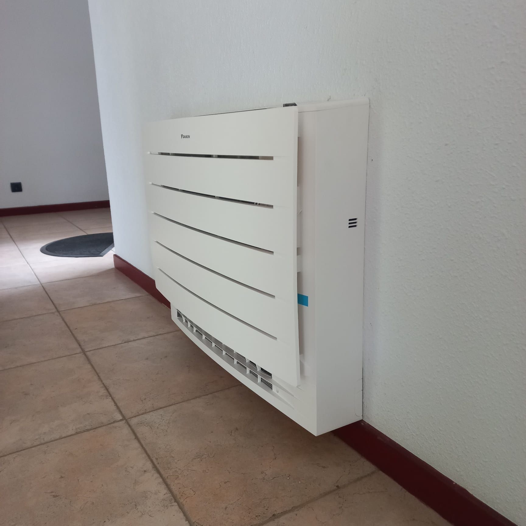 Unité de climatisation blanche montée sur un mur dans une pièce carrelée.