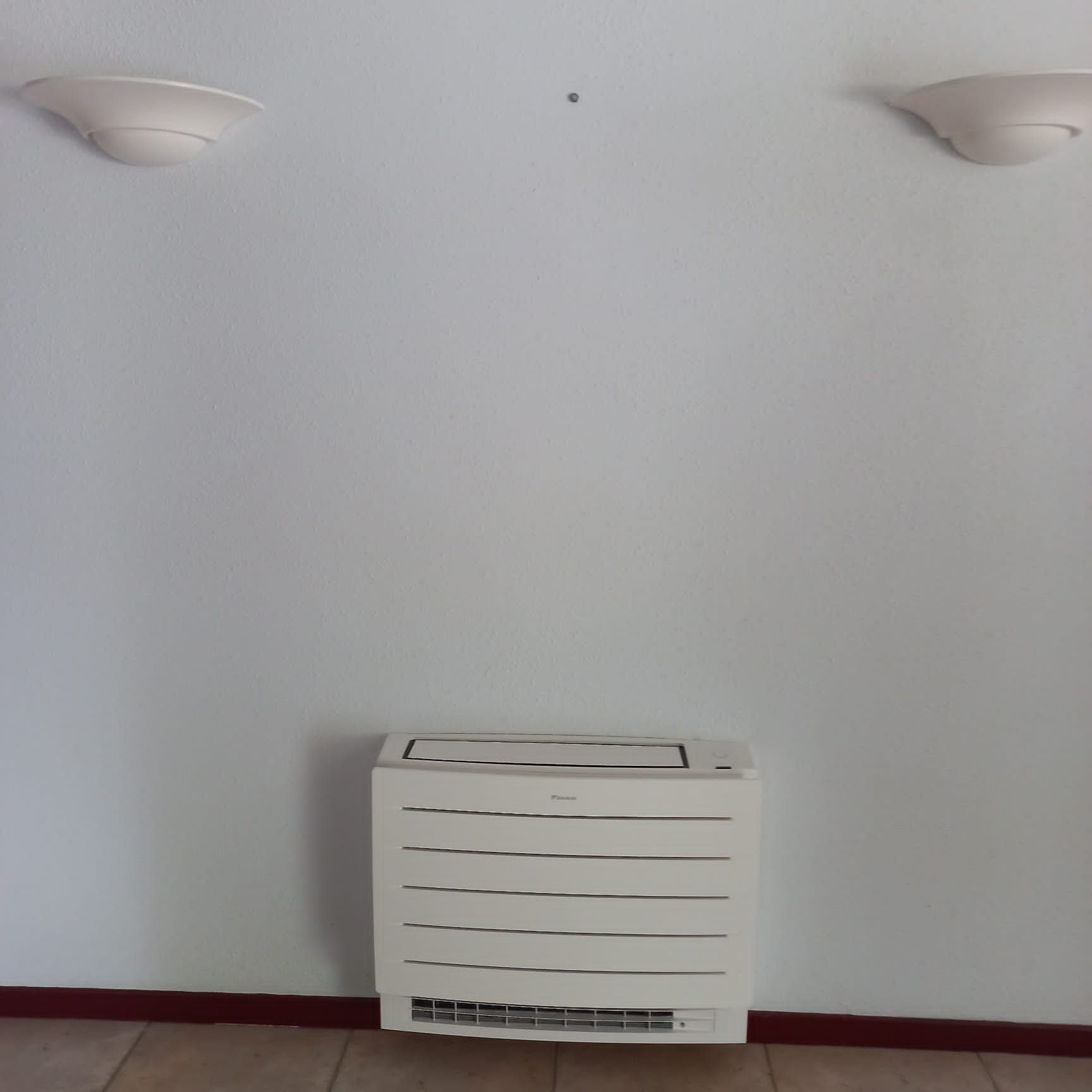 Mur blanc avec deux appliques, climatiseur et plinthe foncée.