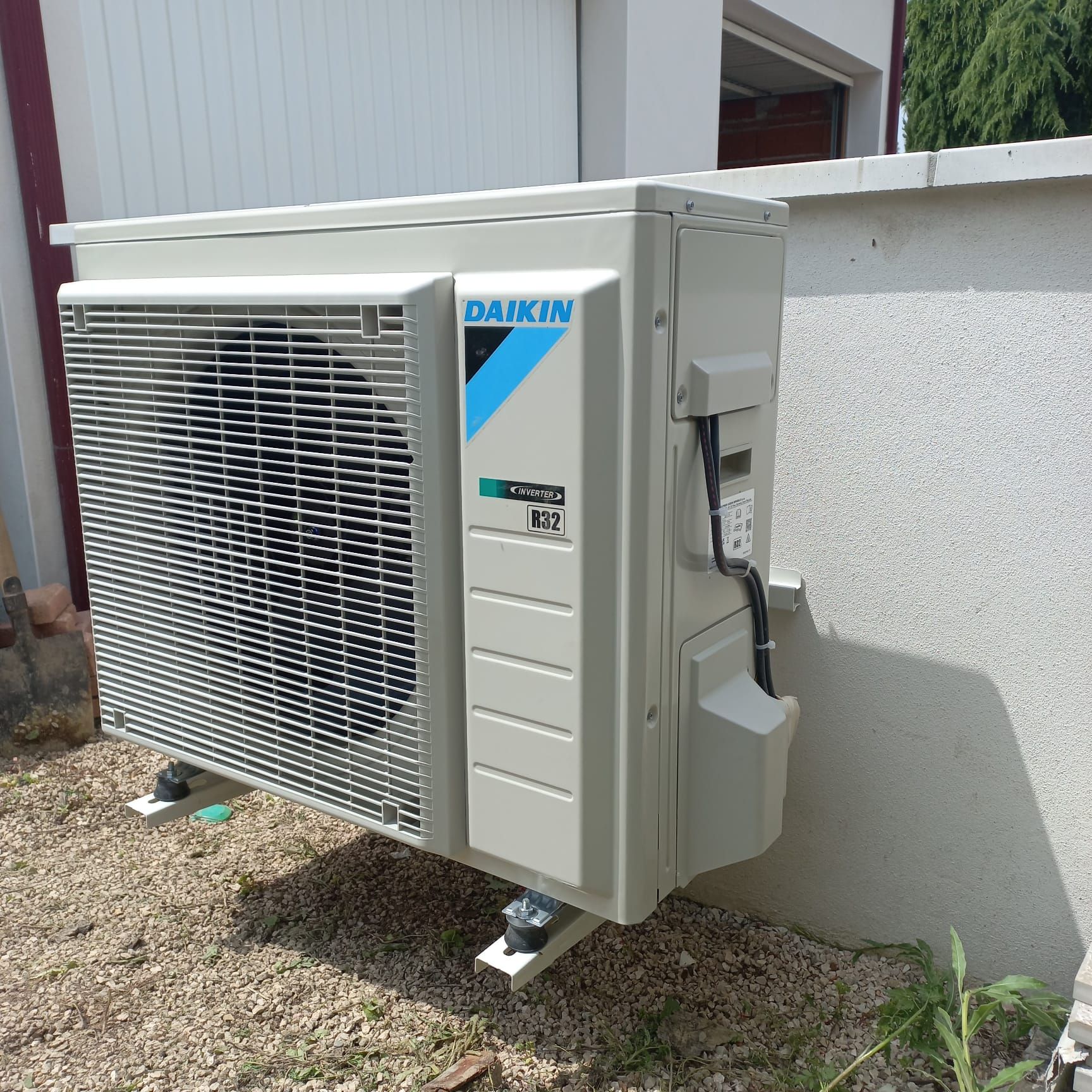Unité de pompe à chaleur Daikin montée sur un support à l'extérieur, à côté d'un mur de couleur claire.