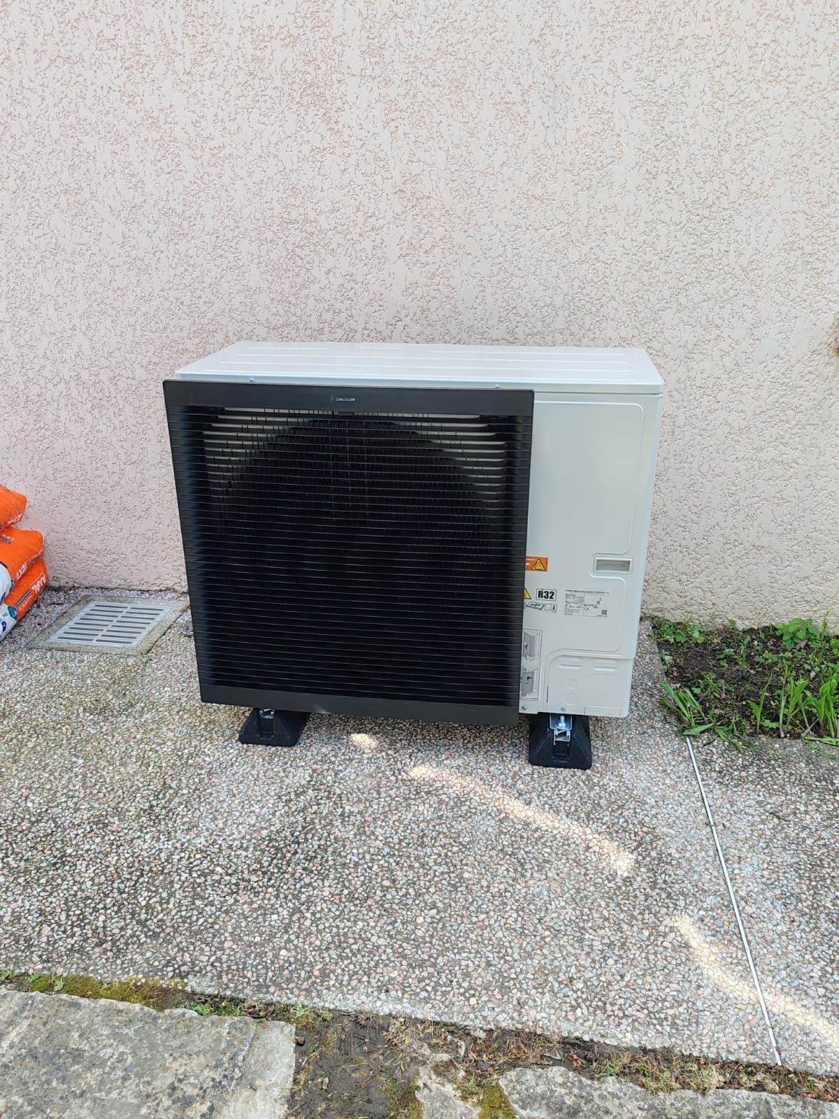 Unité de pompe à chaleur à l'extérieur sur une surface en béton, contre un mur en stuc.