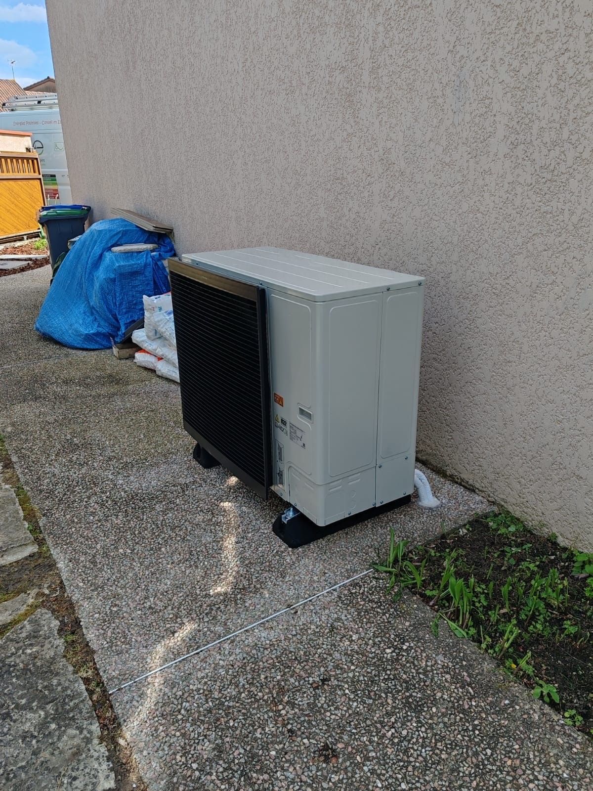 Unité CVC grise contre un mur de couleur claire, avec une grille noire.