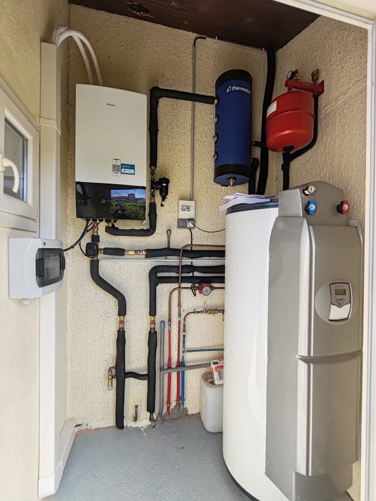 Système de chaudière blanche avec réservoirs et tuyaux sur un mur texturé.