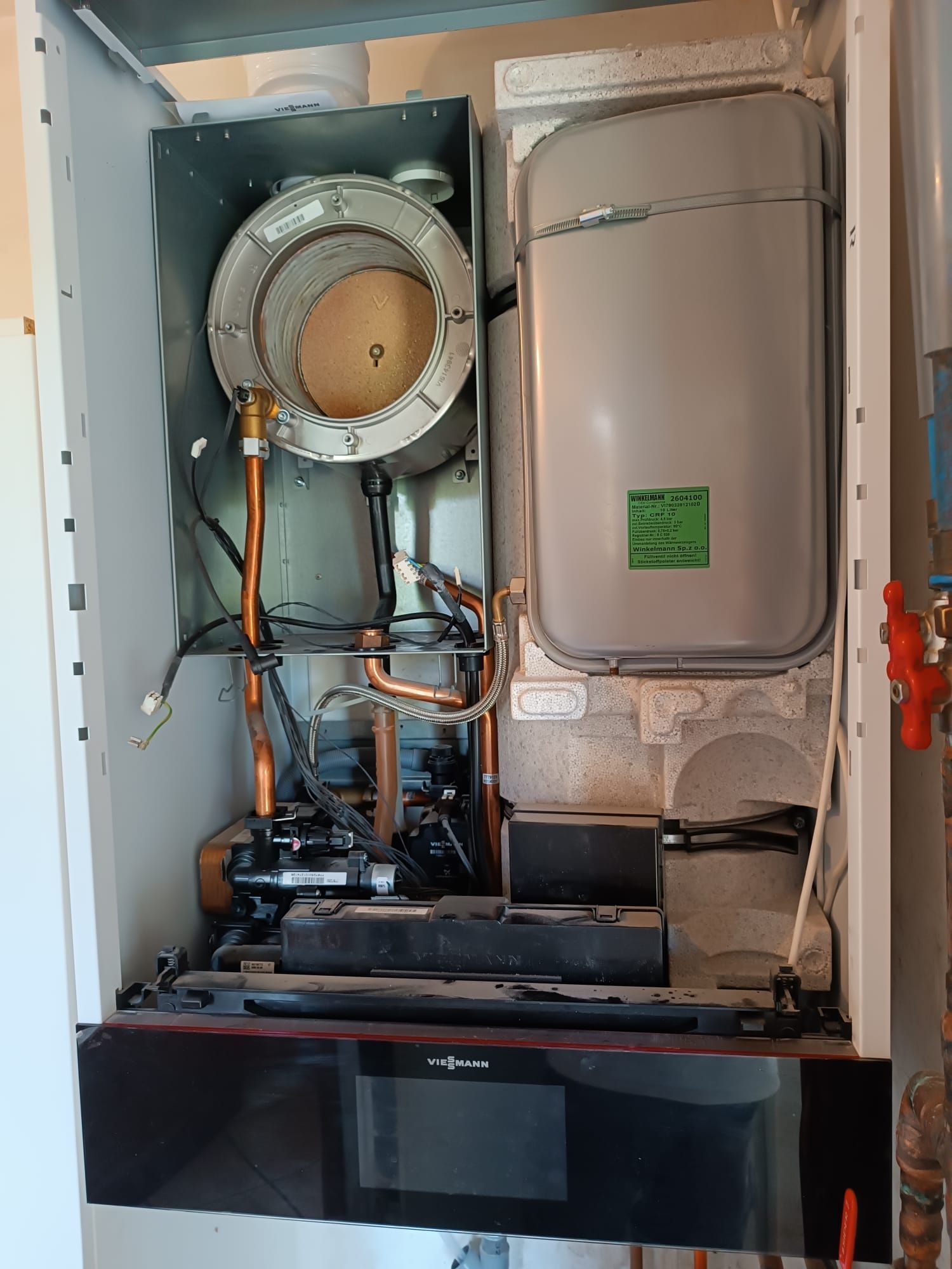 Vue ouverte des composants internes d'une chaudière à gaz, comprenant un échangeur de chaleur, un réservoir d'eau et des tuyaux en cuivre dans un boîtier blanc.