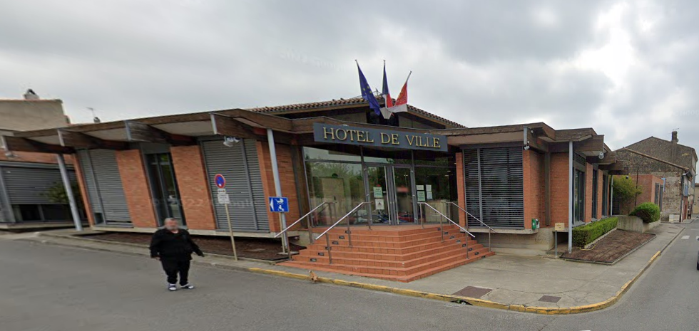 Une personne marche devant une mairie avec une façade en briques, des marches et un drapeau français.
