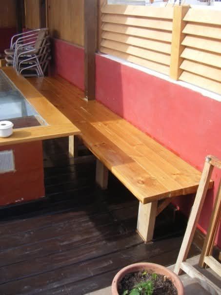 Banco de madera junto a una mesa en un restaurante con paredes rojas y suelo de madera oscura.