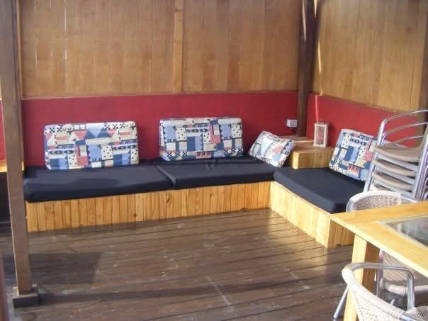 Banco esquinero con paneles de madera, cojines oscuros, almohadas estampadas y paredes rojas en una habitación rústica.