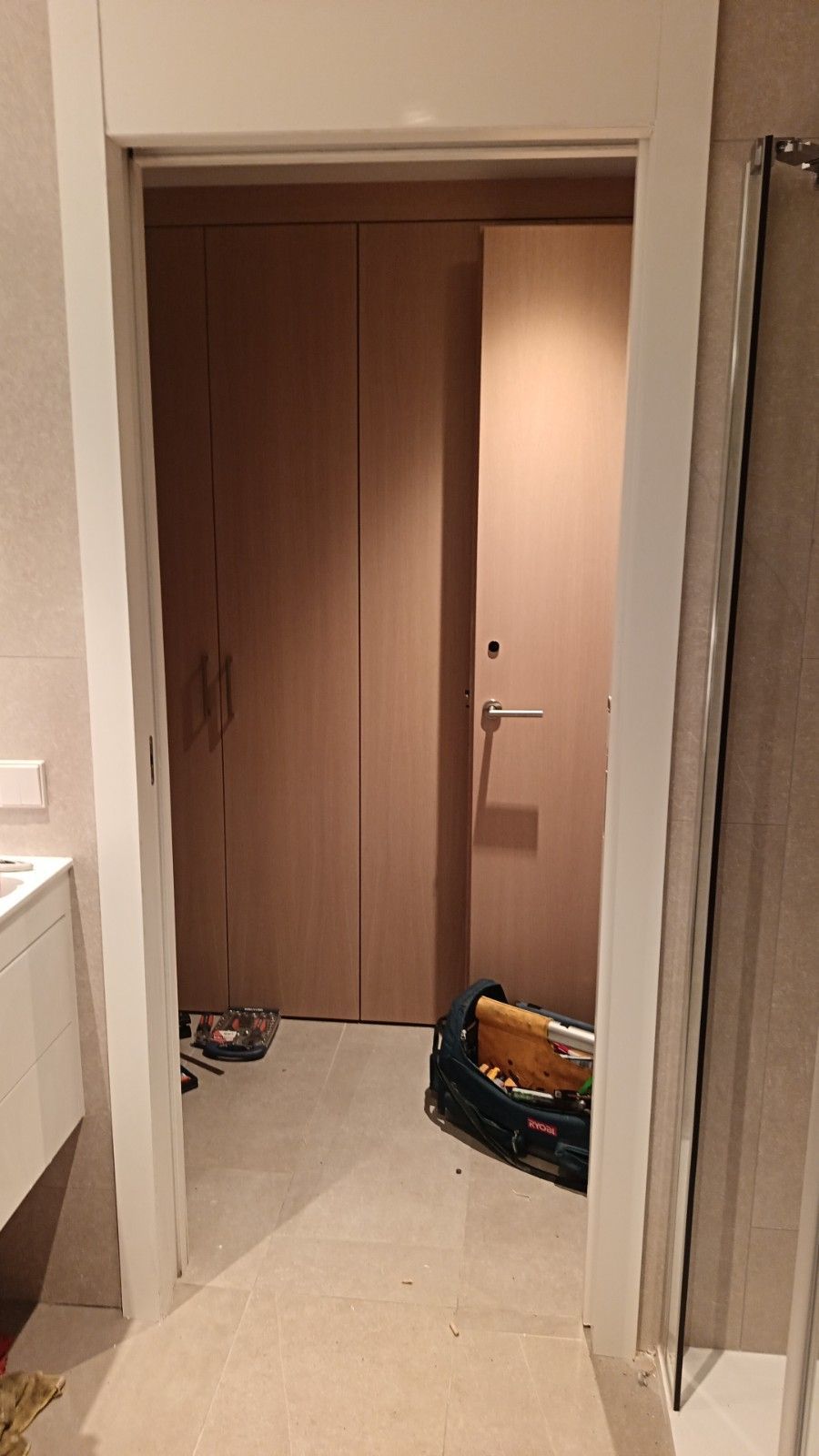 Pasillo con puerta de madera, suelo de baldosas beige y una bolsa en el suelo cerca de la puerta.