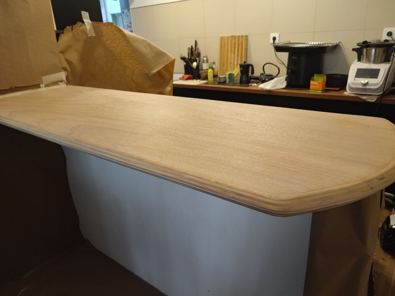 Mesa de trabajo larga cubierta con tela color canela en un taller o sala de manualidades.