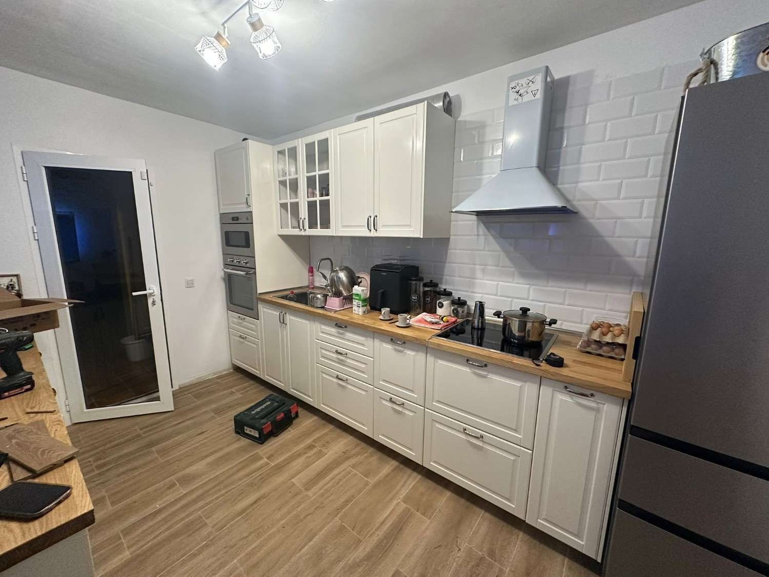 Cocina luminosa con armarios blancos, encimeras de madera, salpicadero gris y frigorífico de acero inoxidable.