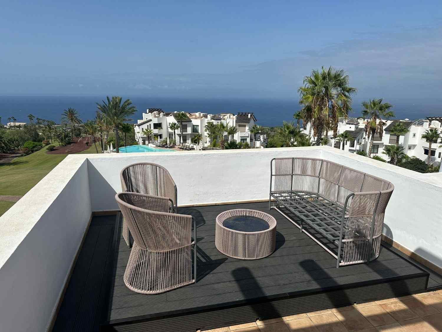 Terraza con vistas a un complejo turístico costero y al océano bajo un cielo azul despejado.