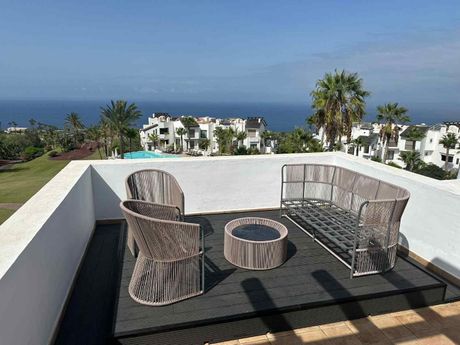 Patio con sillas de mimbre y mesa redonda con vistas a la piscina y al océano.