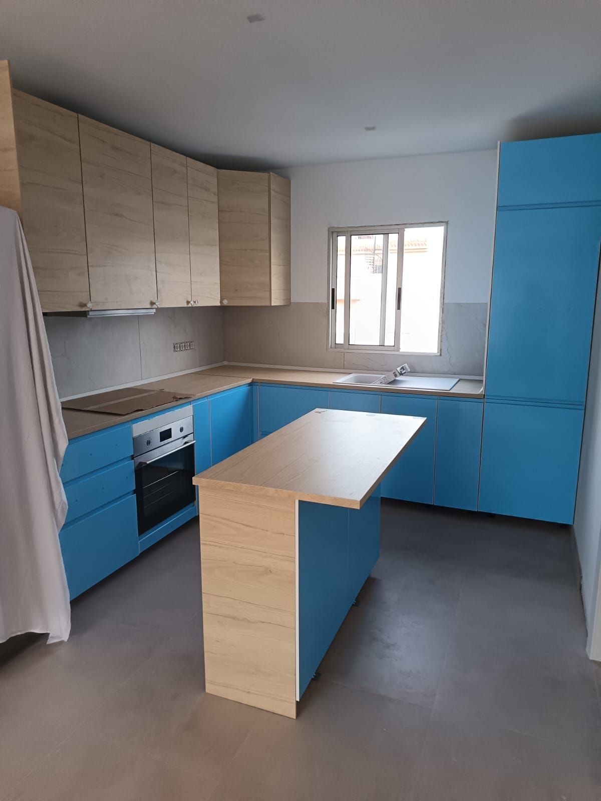 Cocina moderna con armarios azules y de madera, isla blanca y una ventana sobre el fregadero.