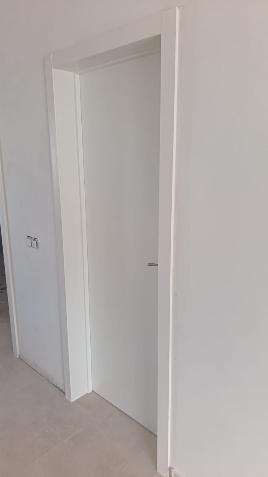 Entrada interior blanca en una habitación sencilla y vacía con paredes claras y moqueta.