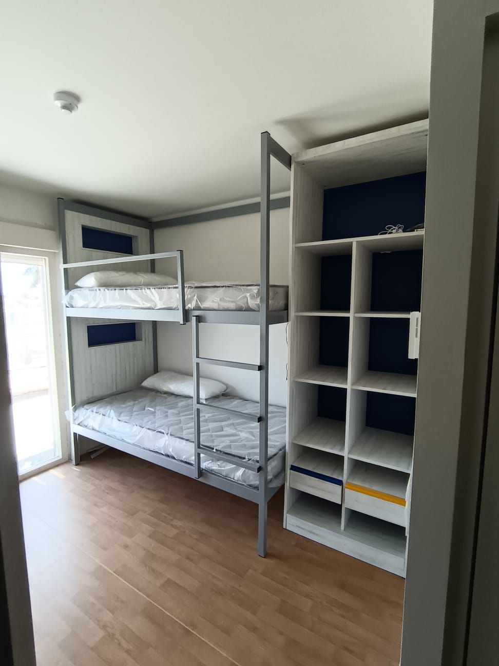Dormitorio con litera gris y estantería blanca, suelo de madera y detalles en azul en las paredes.