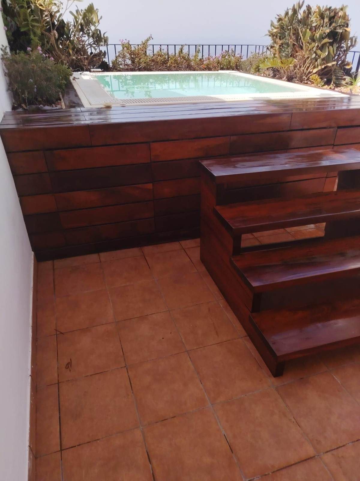 Escaleras de madera que conducen a una pequeña piscina en un patio con vista al océano más allá de la barandilla.