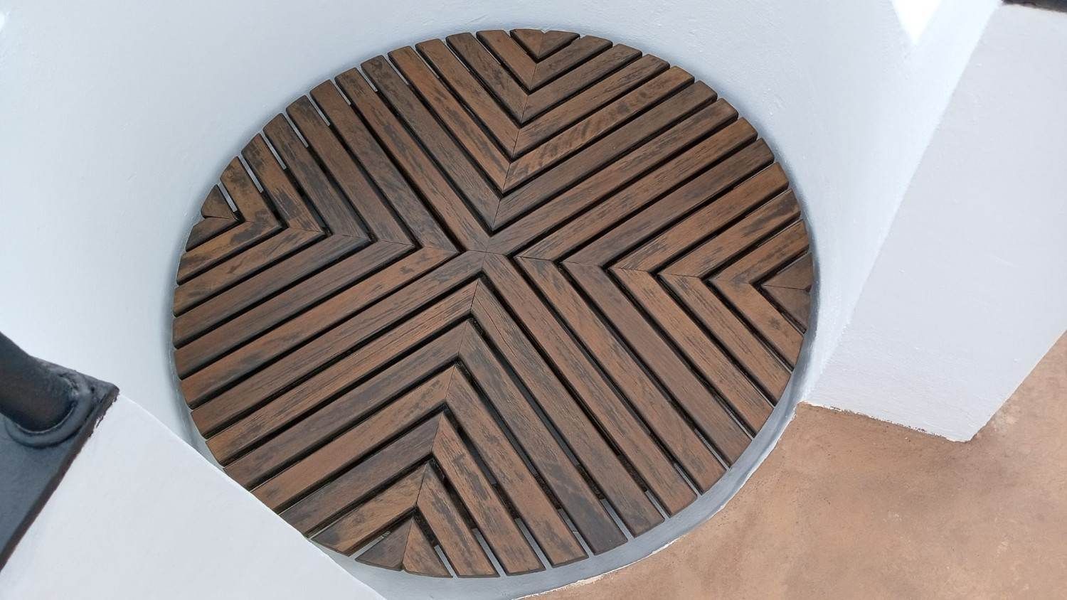 Alfombra redonda de madera con listones en forma de espiga en una esquina blanca sobre un suelo color canela.