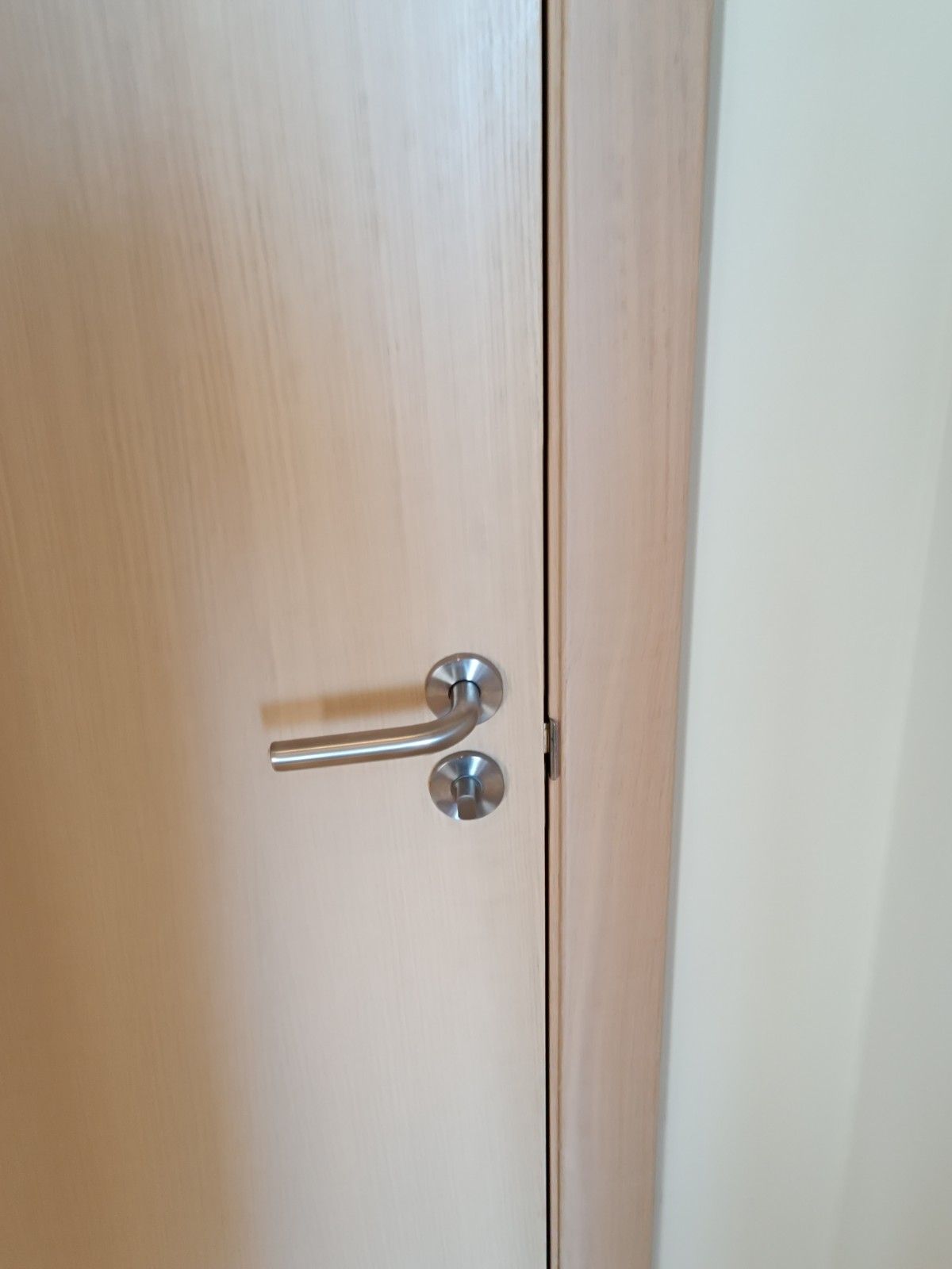 Primer plano de una puerta de madera clara con manilla cromada y cerradura redonda.