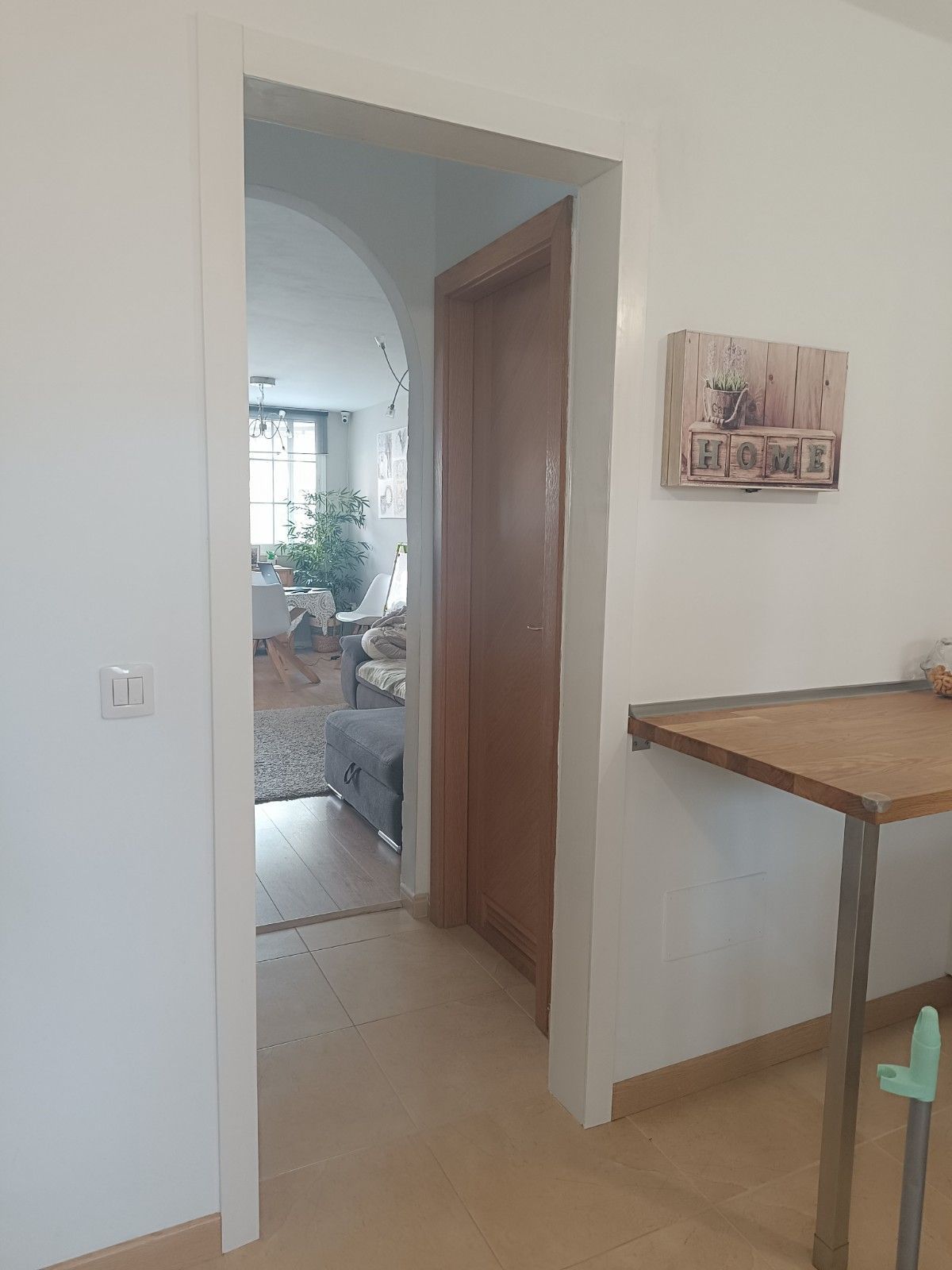 Pasillo interior con puertas abiertas, paredes de color beige y una mesa de madera junto a una puerta blanca.