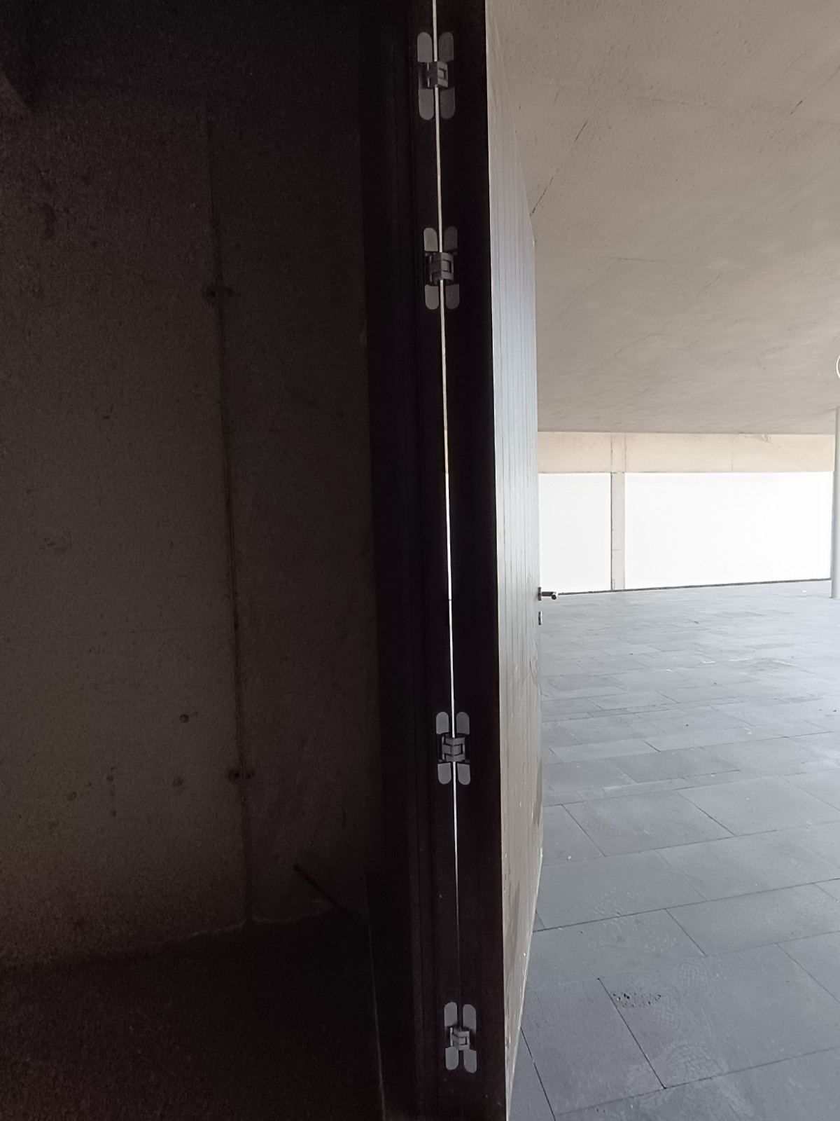 Pasillo con poca luz que da a un balcón exterior luminoso, con un marco de puerta oscuro a la izquierda.