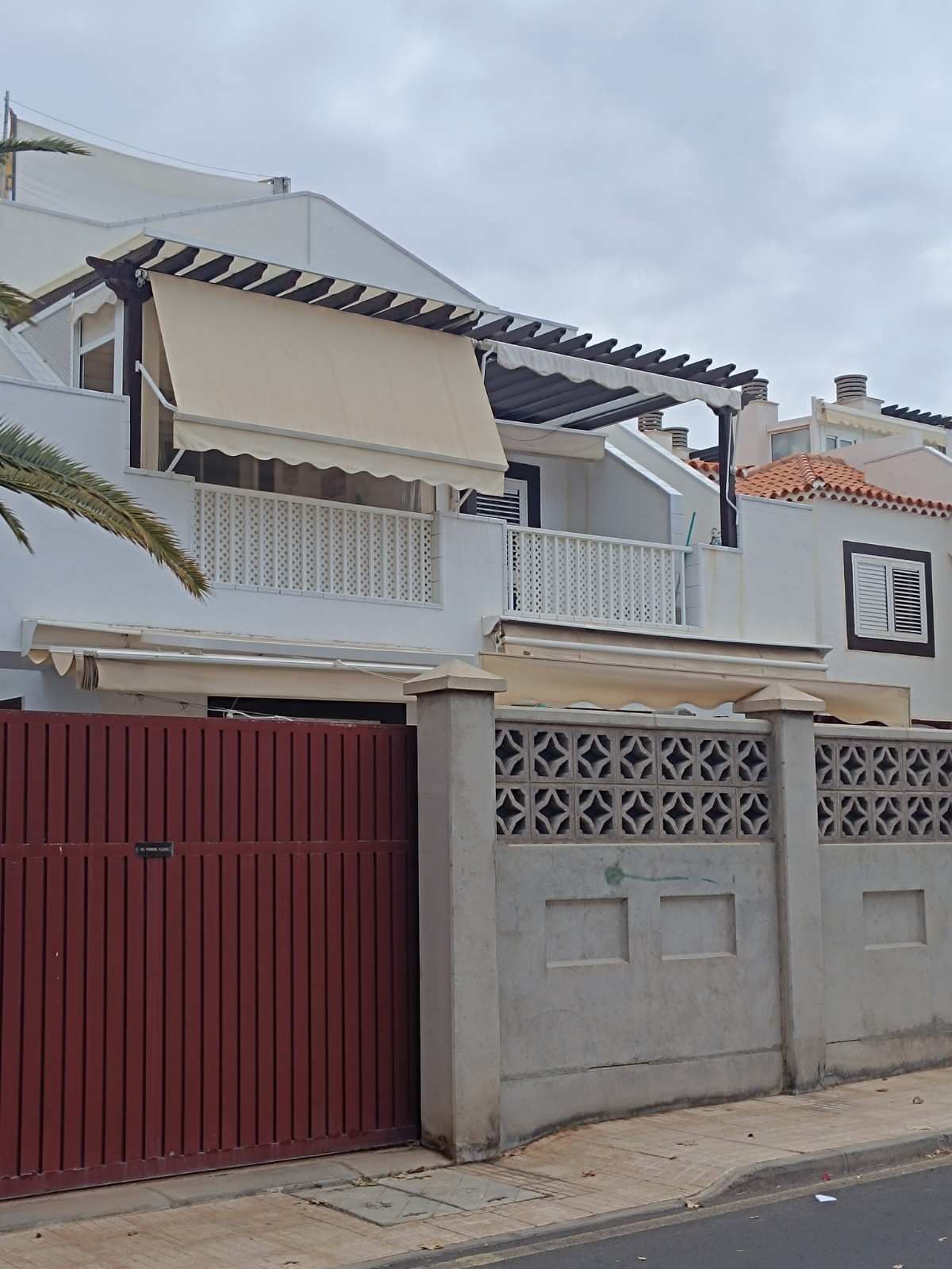 Casa blanca de dos plantas con puerta roja, paredes grises y un pequeño balcón cubierto en una calle.