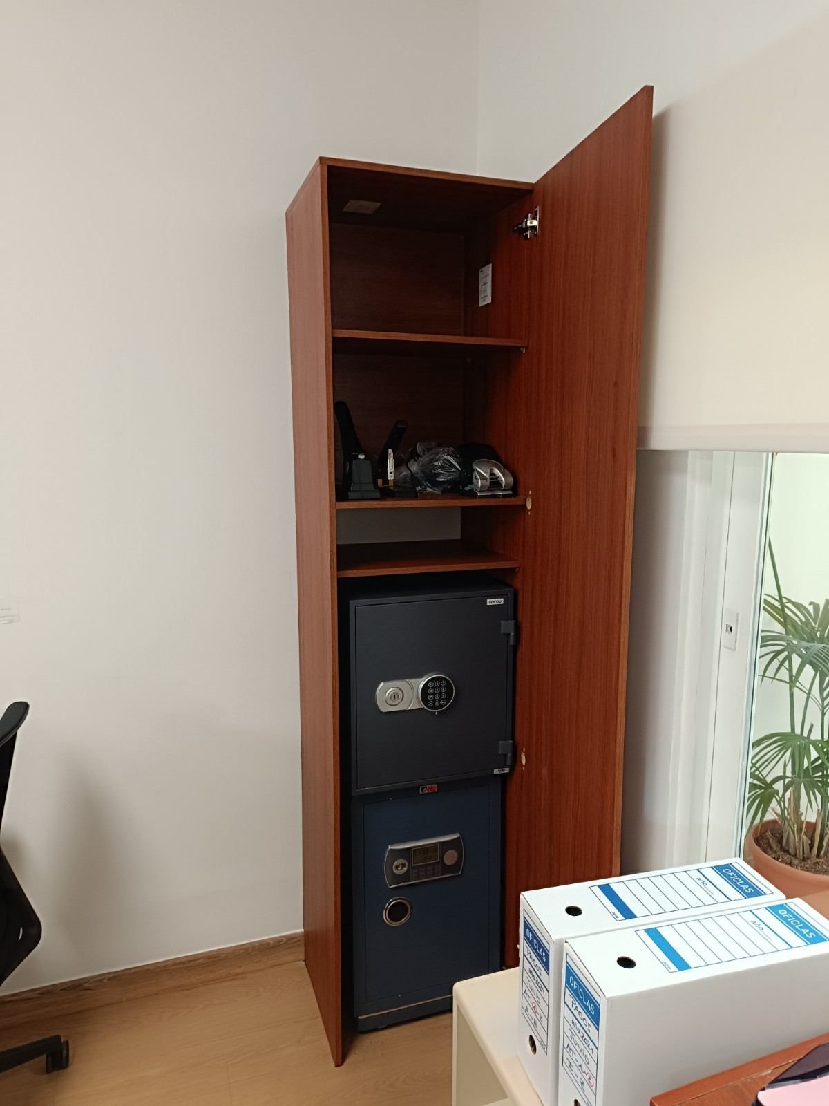 Armario de madera abierto con estantes, equipo fotográfico y una caja fuerte negra; caja de cartón en primer plano.