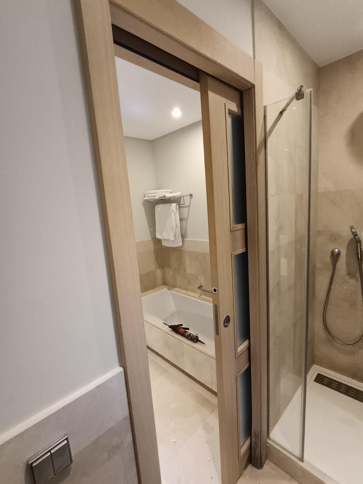 Vista desde la puerta de entrada a un baño moderno con azulejos beige, toallero y cabina de ducha de cristal.