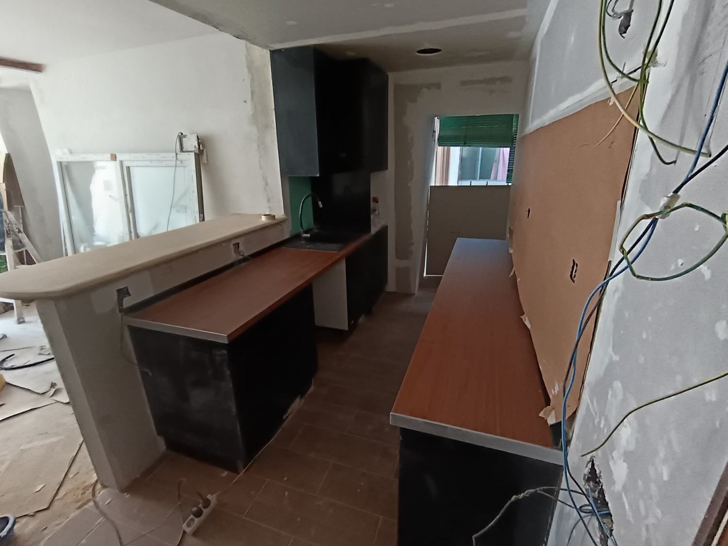 Habitación sin terminar con largos escritorios de madera, cables expuestos y escombros de construcción a lo largo de las paredes.
