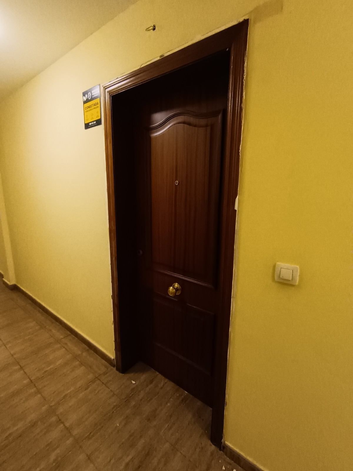 Pasillo oscuro con una puerta de madera oscura cerrada y paredes amarillas.