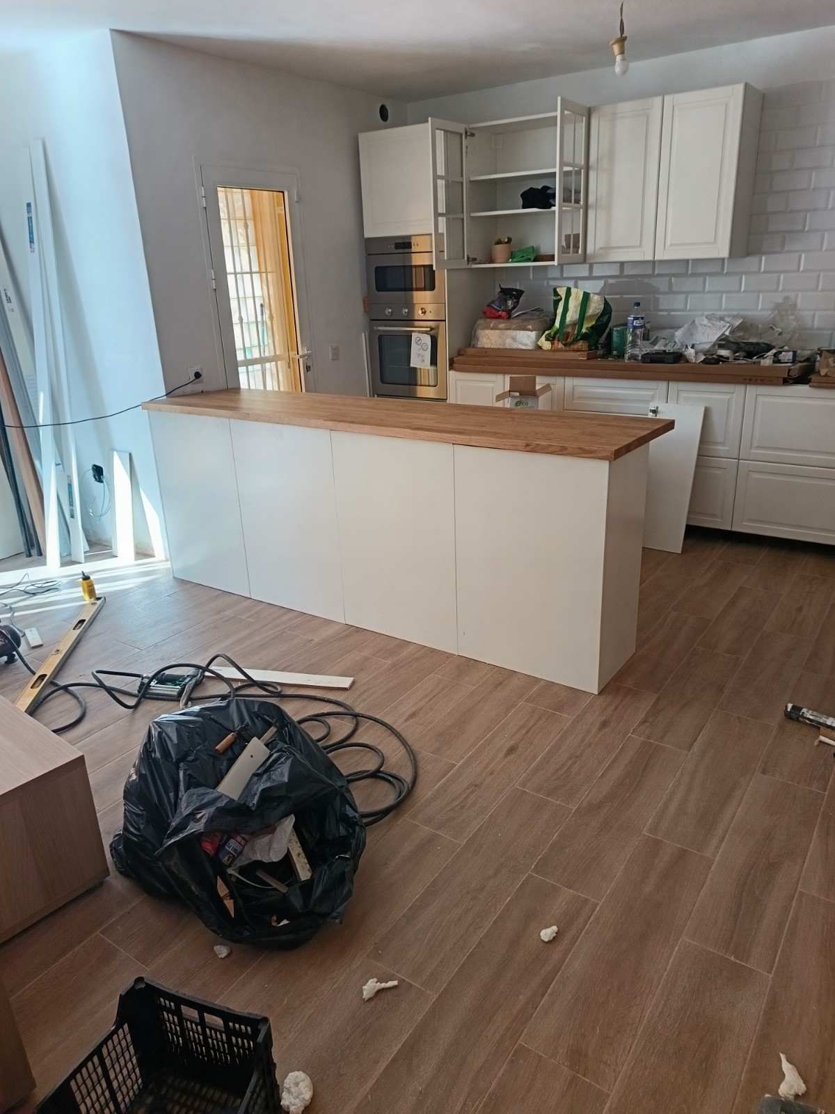 Cocina reformada con armarios blancos, isla de madera y materiales de construcción en el suelo.