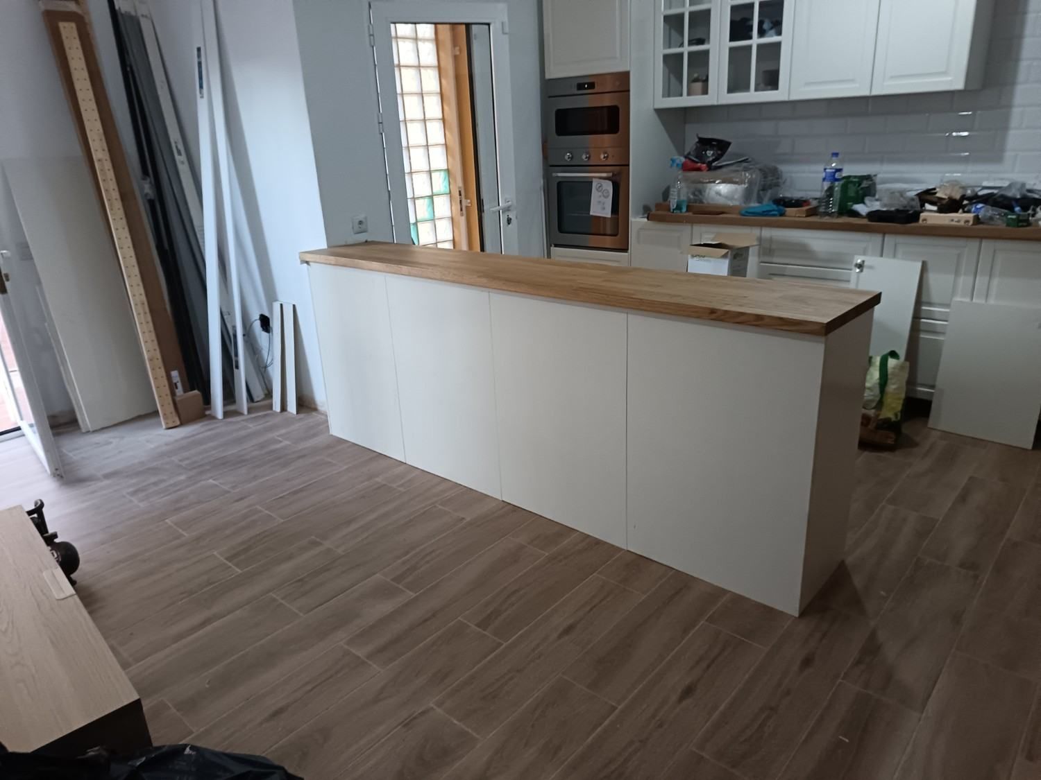 Cocina moderna con isla blanca, encimera de madera, suelo de madera clara y armarios abiertos.