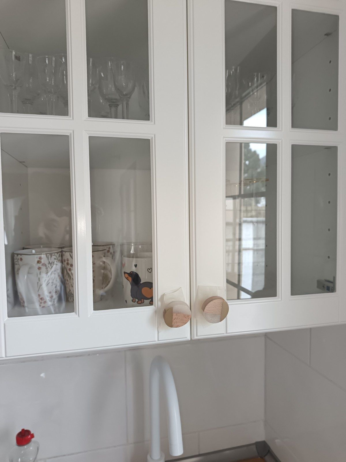 Armarios de cocina blancos con puertas de cristal y tiradores redondos sobre el fregadero y salpicadero de azulejos.
