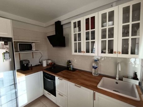 Cocina moderna y luminosa con armarios blancos, encimera de madera, vitrocerámica, fregadero, microondas y armarios con puertas de cristal.