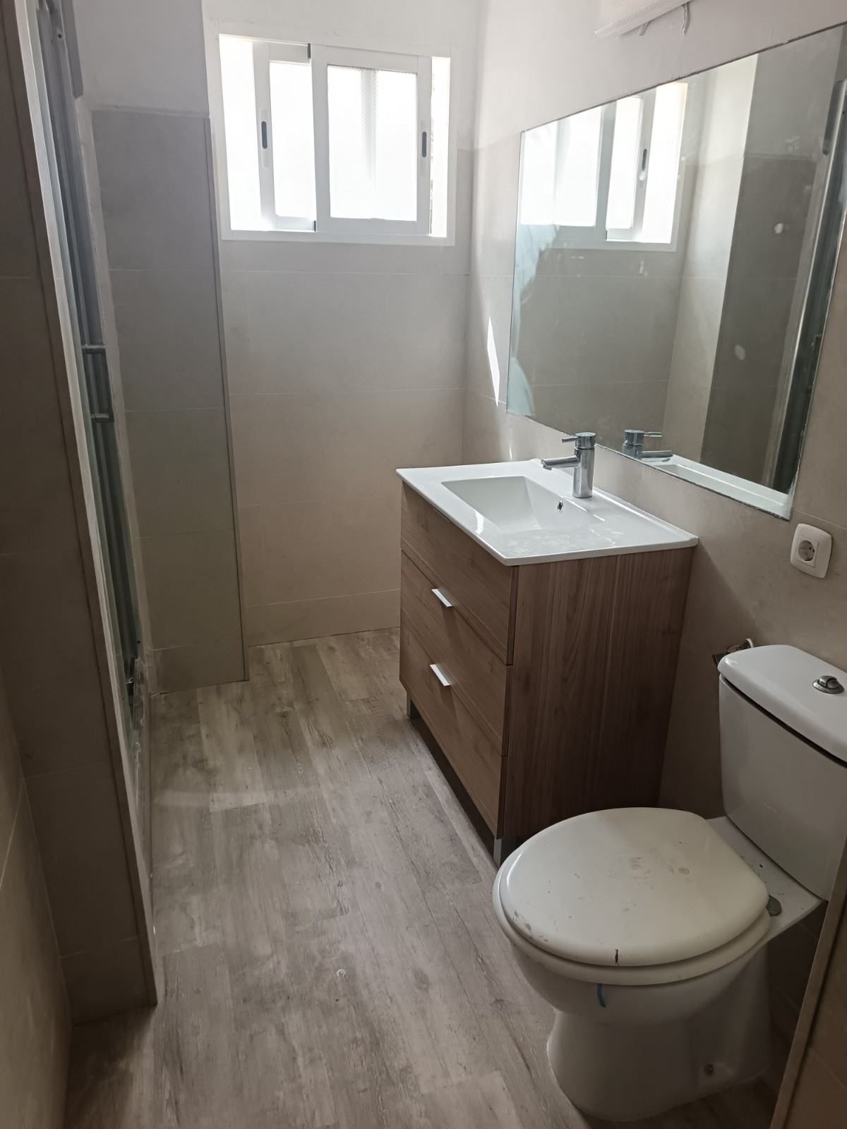 Baño estrecho con inodoro, lavabo de madera, espejo grande y ventana esmerilada.